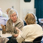 A woman listens intently to another woman who is gesturing; both are seated at a table